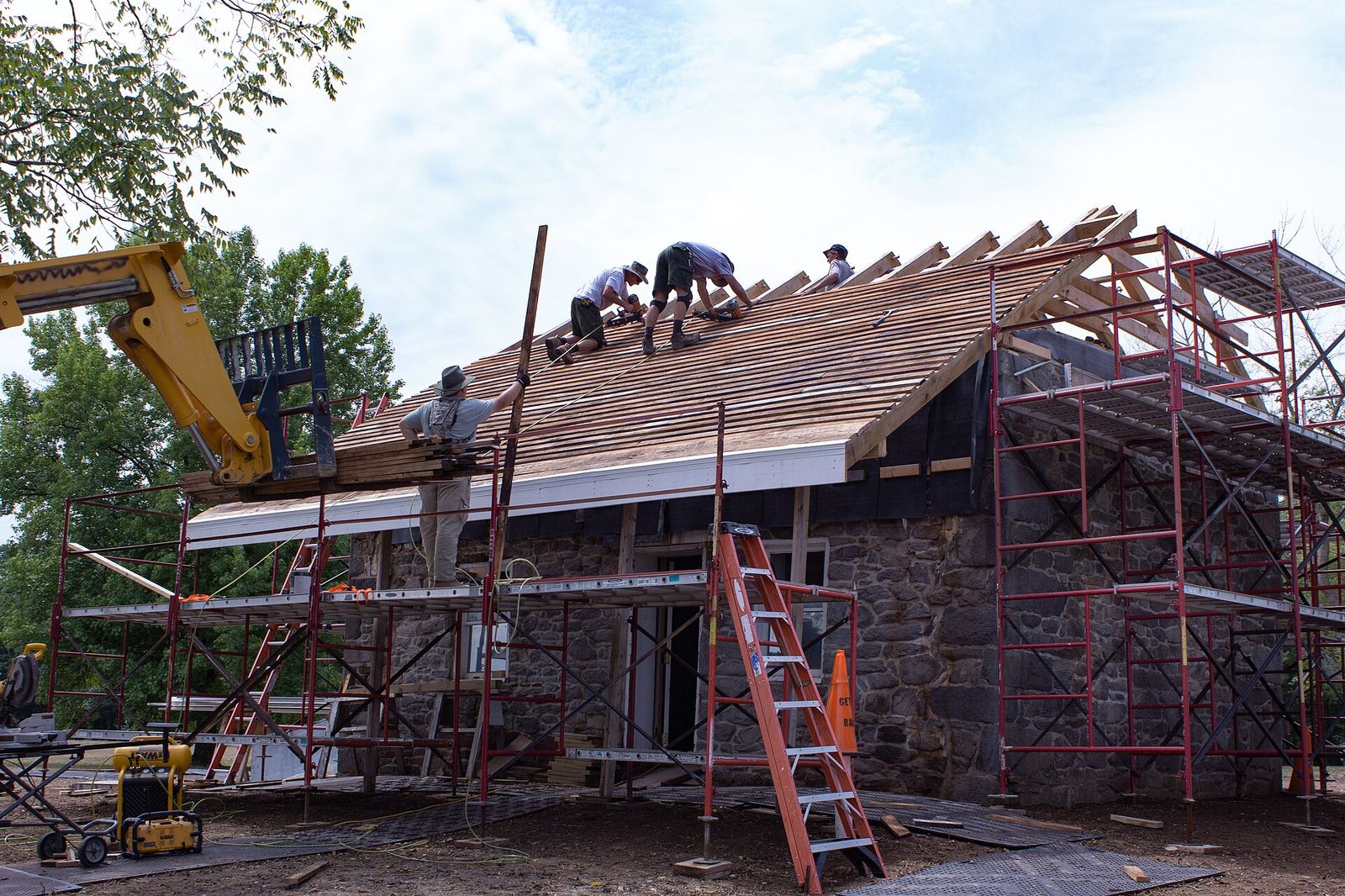 Elm Street Roofing crew decking a steep roof on a stone house in Naperville, telehandler lifting the bundles